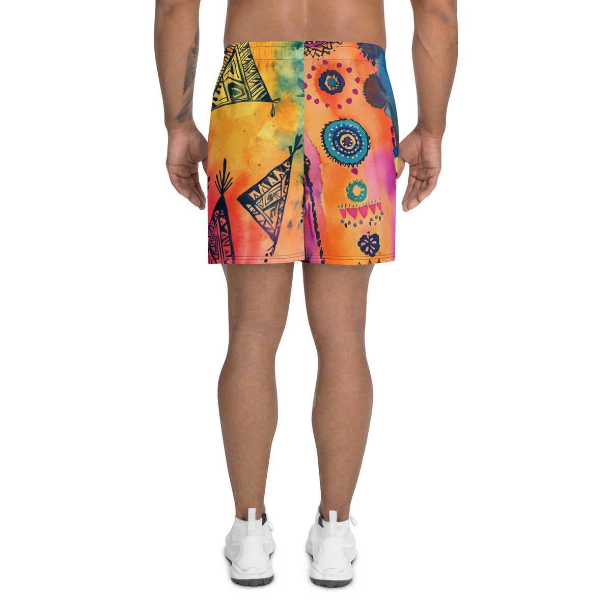 Aztec-inspired long sports shorts featuring a colorful tribal geometric abstract print with triangles, sun-like symbols, dots, decorative linework, and organic motifs in yellow, orange, coral, pink, magenta, purple, turquoise, teal, and navy. Long athletic cut with elastic waistband and white drawstring