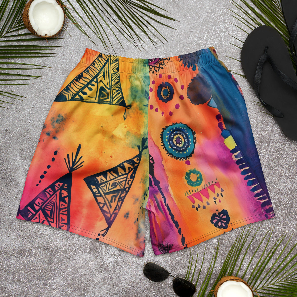 Aztec-inspired long sports shorts featuring a colorful tribal geometric abstract print with triangles, sun-like symbols, dots, decorative linework, and organic motifs in yellow, orange, coral, pink, magenta, purple, turquoise, teal, and navy. Long athletic cut with elastic waistband and white drawstring