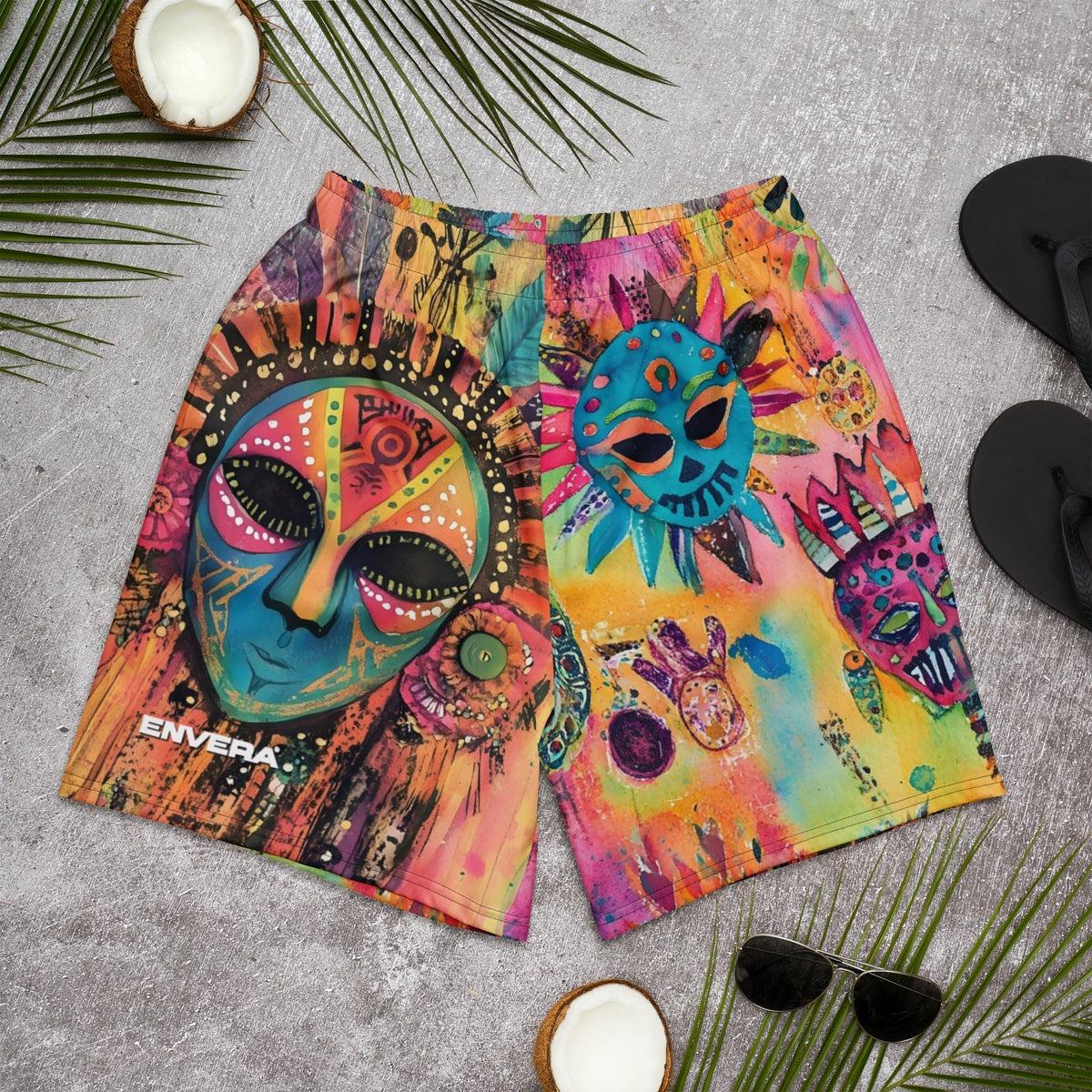 Long sports shorts featuring a vibrant psychedelic tribal mask print with expressive painted faces, decorative folk-art symbols, abstract shapes, brushstrokes, and colorful collage-like textures in turquoise, teal, coral, pink, magenta, orange, yellow, purple, black, and earthy tones. Unisex athletic design with a longer cut, elastic waistband, and bold artistic all-over pattern