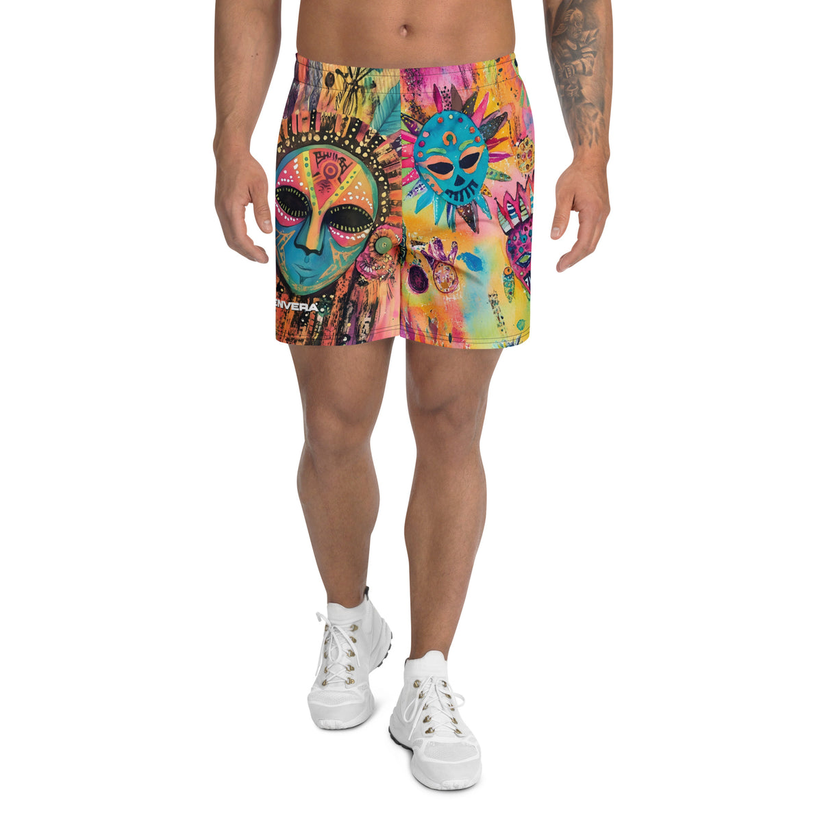Long sports shorts featuring a vibrant psychedelic tribal mask print with expressive painted faces, decorative folk-art symbols, abstract shapes, brushstrokes, and colorful collage-like textures in turquoise, teal, coral, pink, magenta, orange, yellow, purple, black, and earthy tones. Unisex athletic design with a longer cut, elastic waistband, and bold artistic all-over pattern